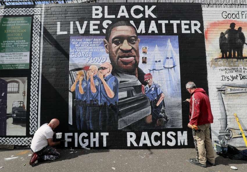 NOTE: GRAPHIC CONTENT ON MURAL | Artists Lyonsie, left, and Micky Doc put the finishing touches to a mural to George Floyd at Belfast's International Wall on the Falls Road. The mural was commissioned by Feile an Phobail and Failte Feirste Thiar.