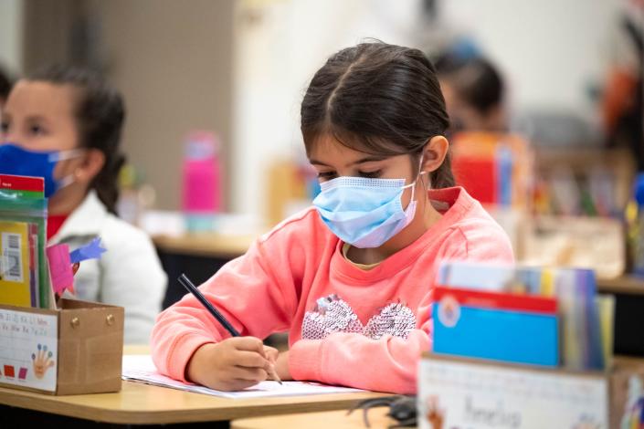 student wearing masks writes on paper