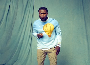 Kevin Hart points at the camera while wearing a blue Victor Li sweater with a yellow hot air balloon on it.