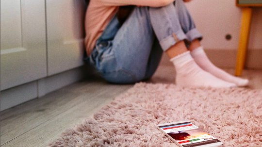 Girl sitting with her head in her knees with her phone lying face-up.