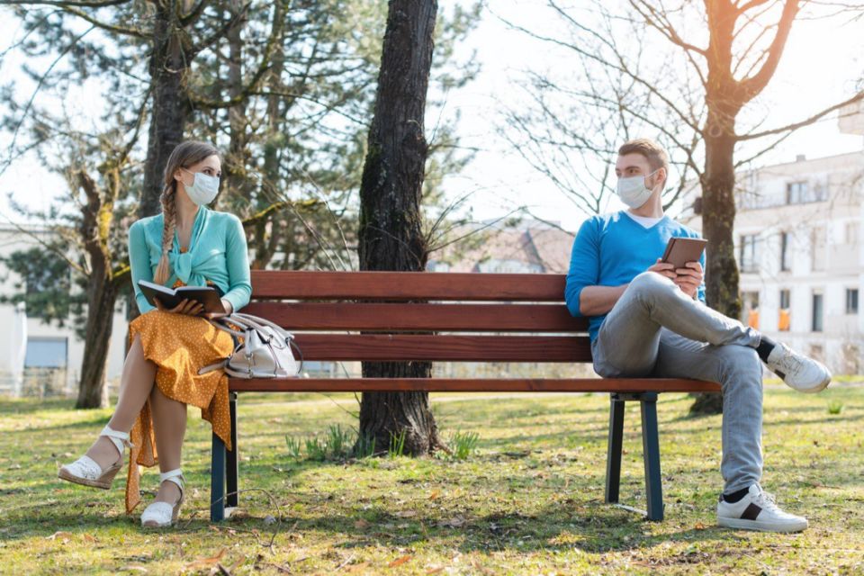 Woman and man in social distancing sitting on bench in park