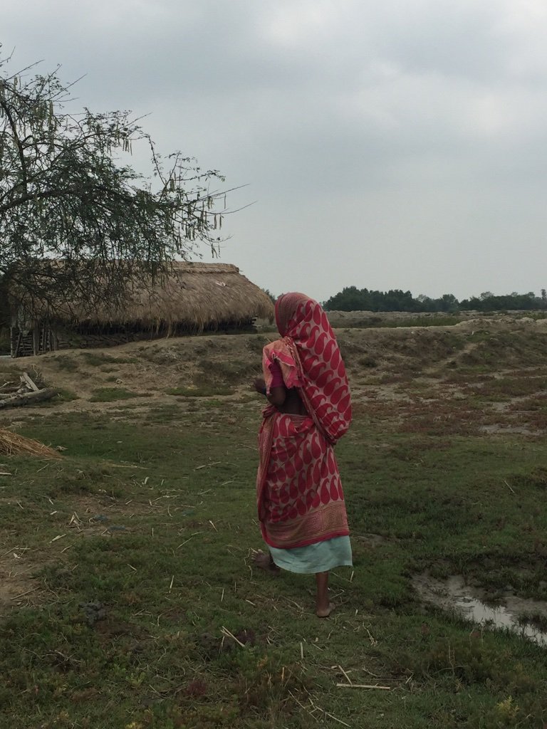 A woman dressed in a pink sari walks across a field.