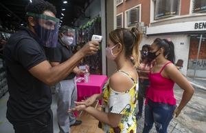 A mask-wearing shopper gets her temperature checked before entering a store (AP/Andre Penner)