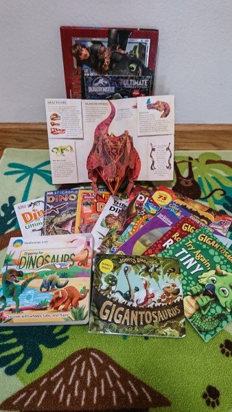 Multiple dinosaur books sit on a green carpet.