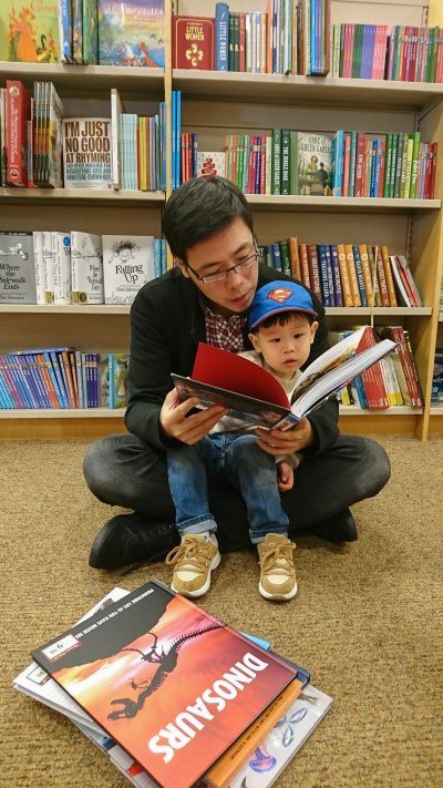A man reads a book to his son who is sitting on his lap.